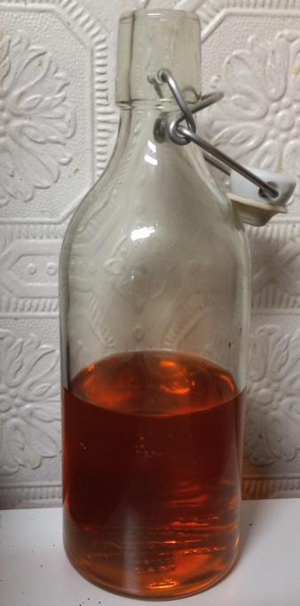 A clear glass bottle with an integrated stopper hanging off the side half-full of a transparent pink liquid, roughly the color of rosé.