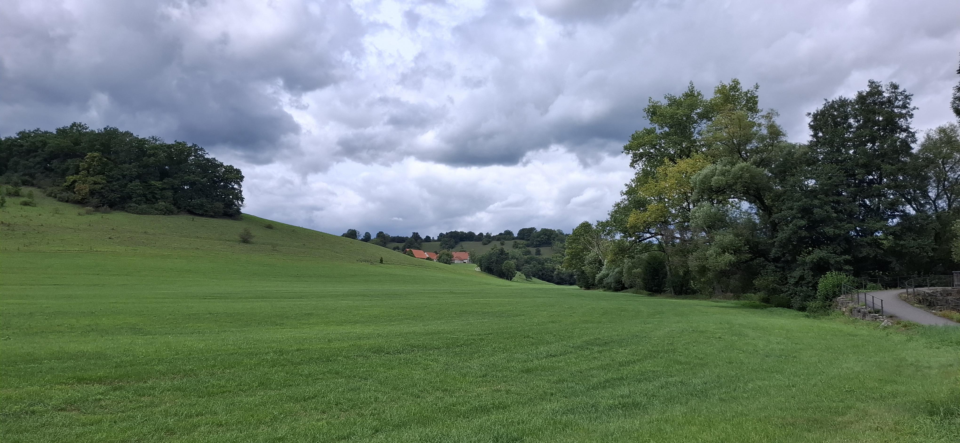 Kocher valley. Meadowy countryside. Farm buildings appear at the horizon behind the next bent of the river.